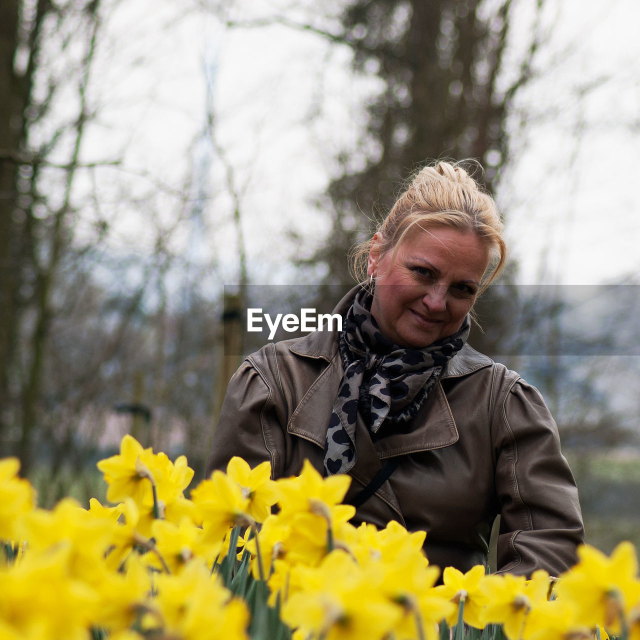 Portrait of smiling woman standing by yellow flowers at park