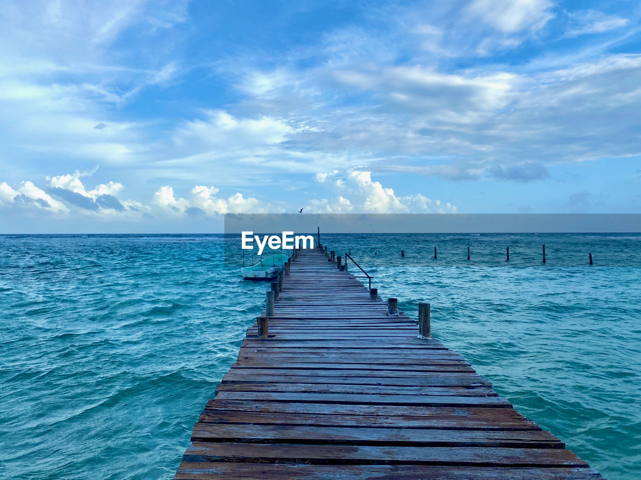 Wooden jetty leading to pier over sea against sky