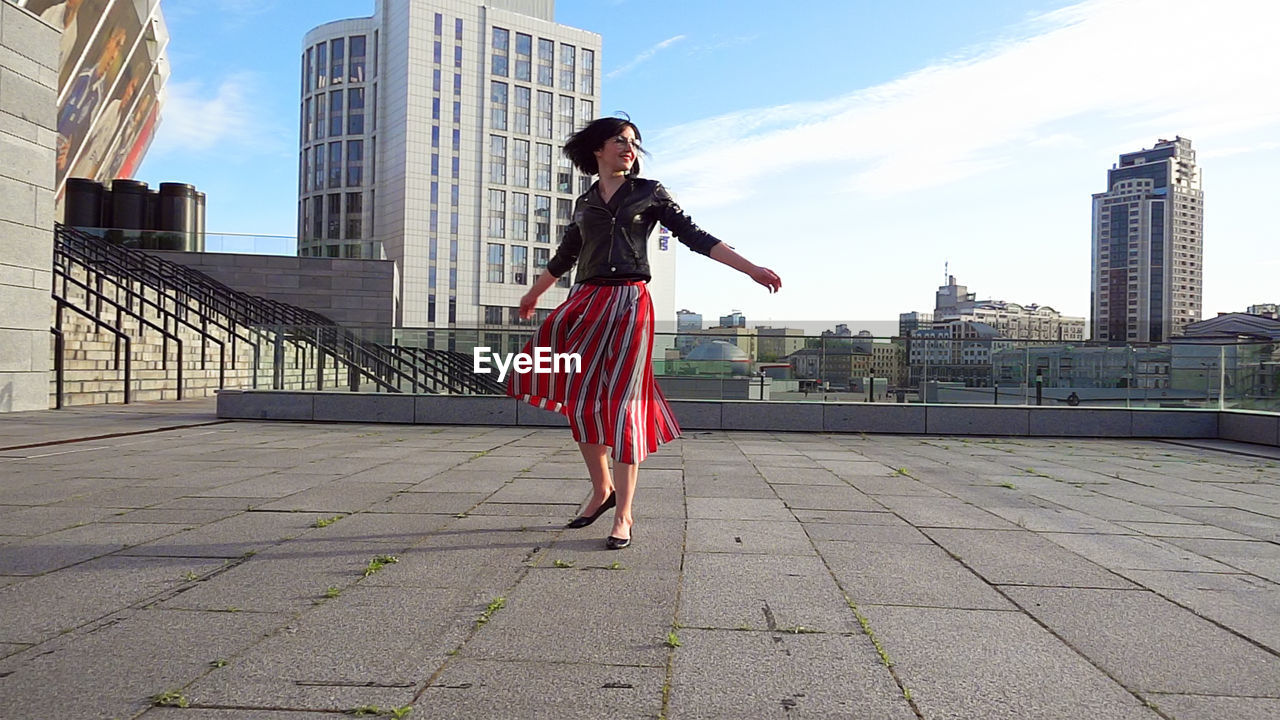 Happy woman wearing striped skirt and jacket on footpath in city