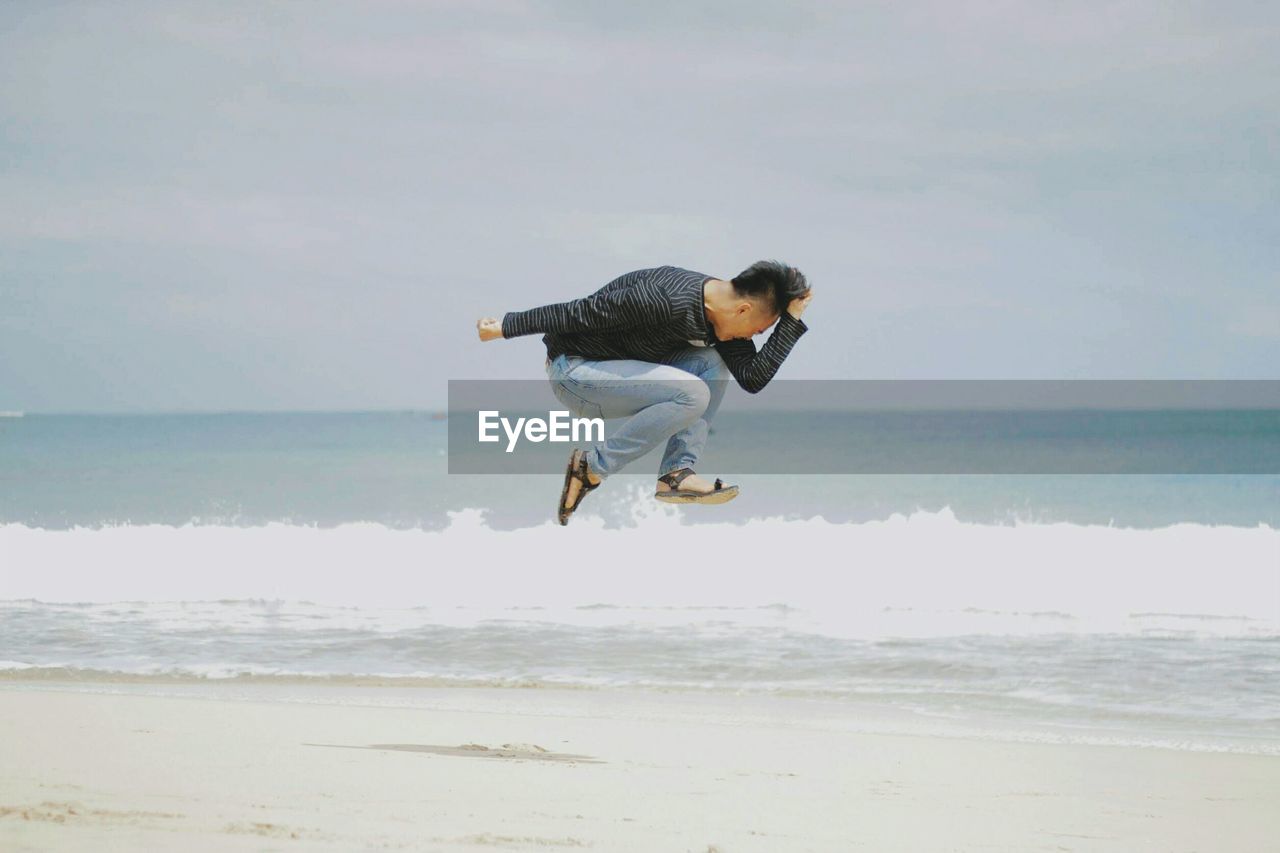 Man jumping at beach against sky