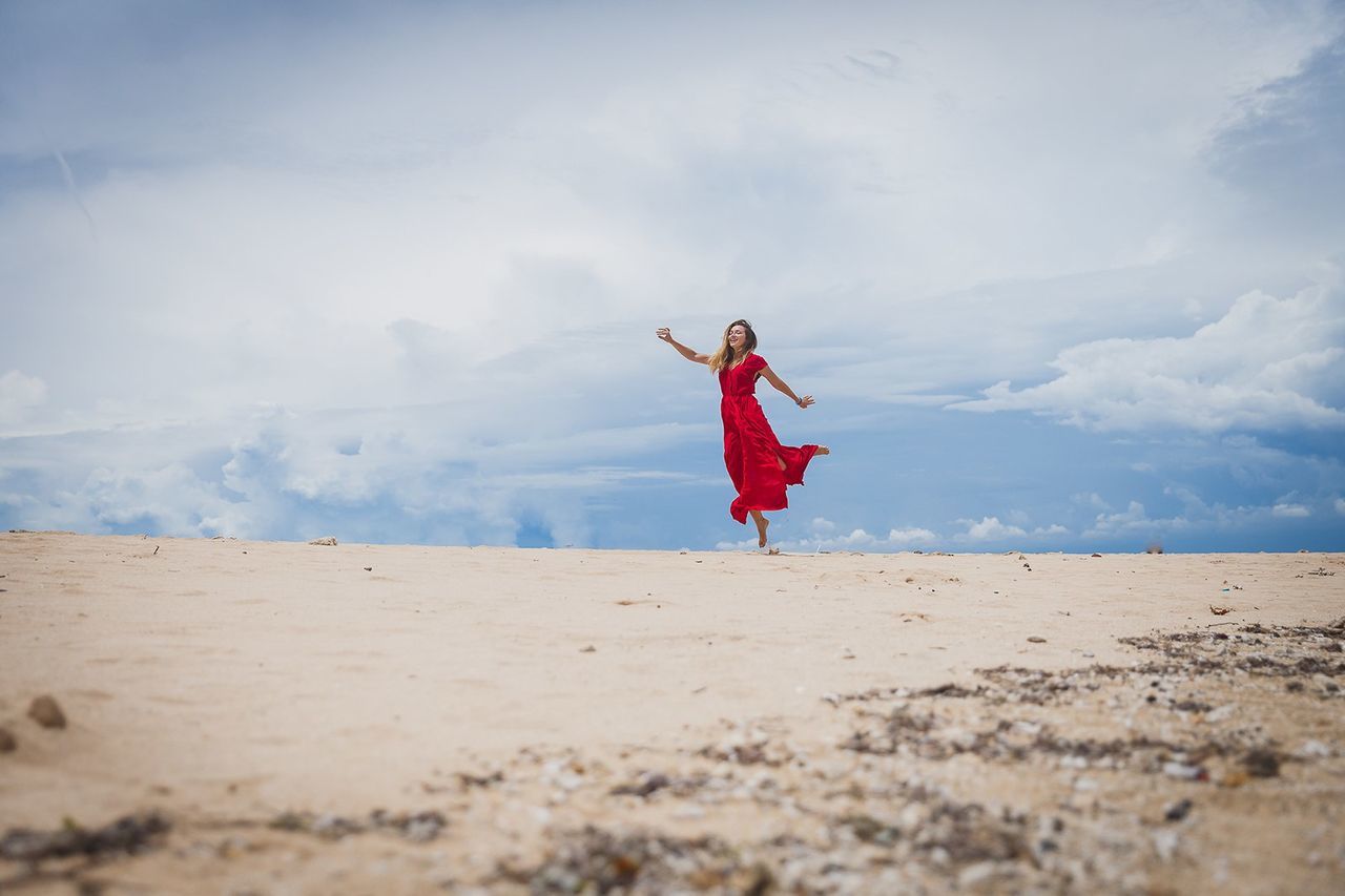Woman dancing on sand at beach against sky