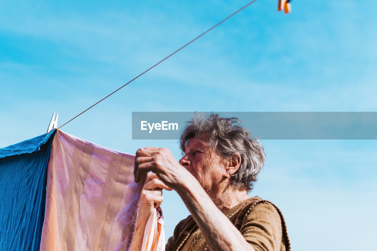 Woman drying laundry on clothesline against blue sky