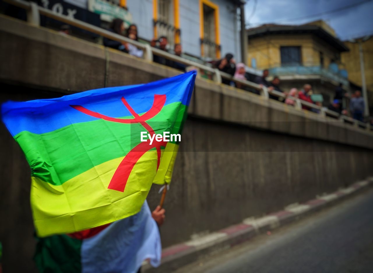 MIDSECTION OF MAN HOLDING COLORFUL UMBRELLA IN CITY