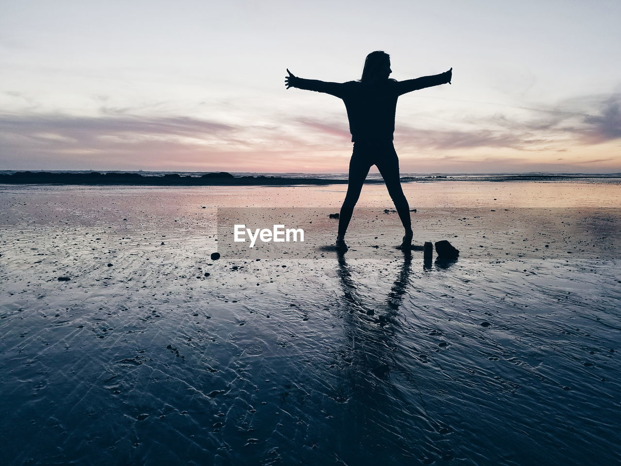 Silhouette woman standing with arms outstretched at beach during sunset