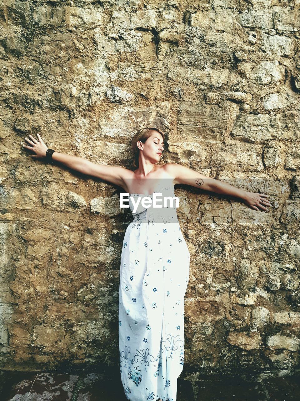 Woman with arms outstretched and eyes closed standing against wall