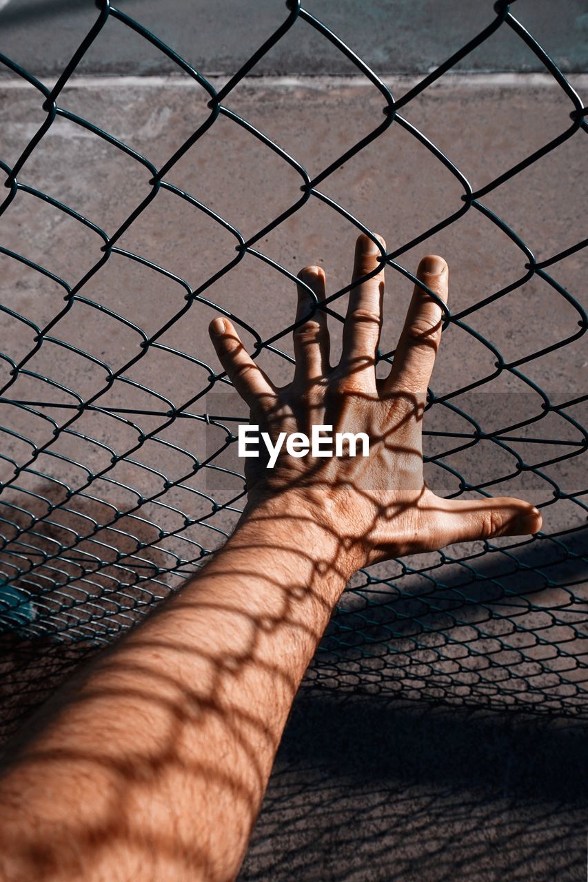 Hand with shadow shapes grabbing a metallic fence