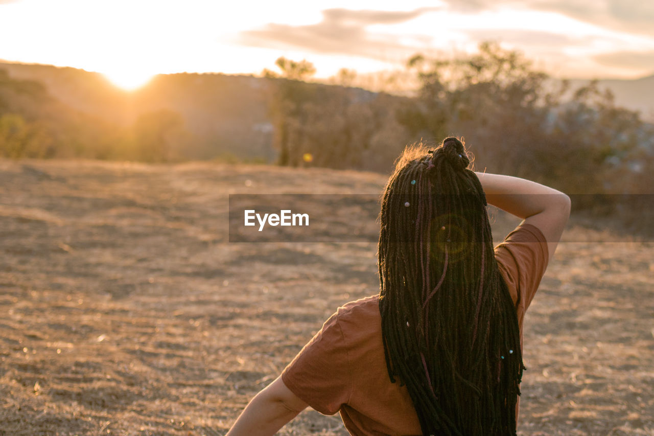 Young woman is sitting in the lotus position and doing yoga on mountain top, back view. 