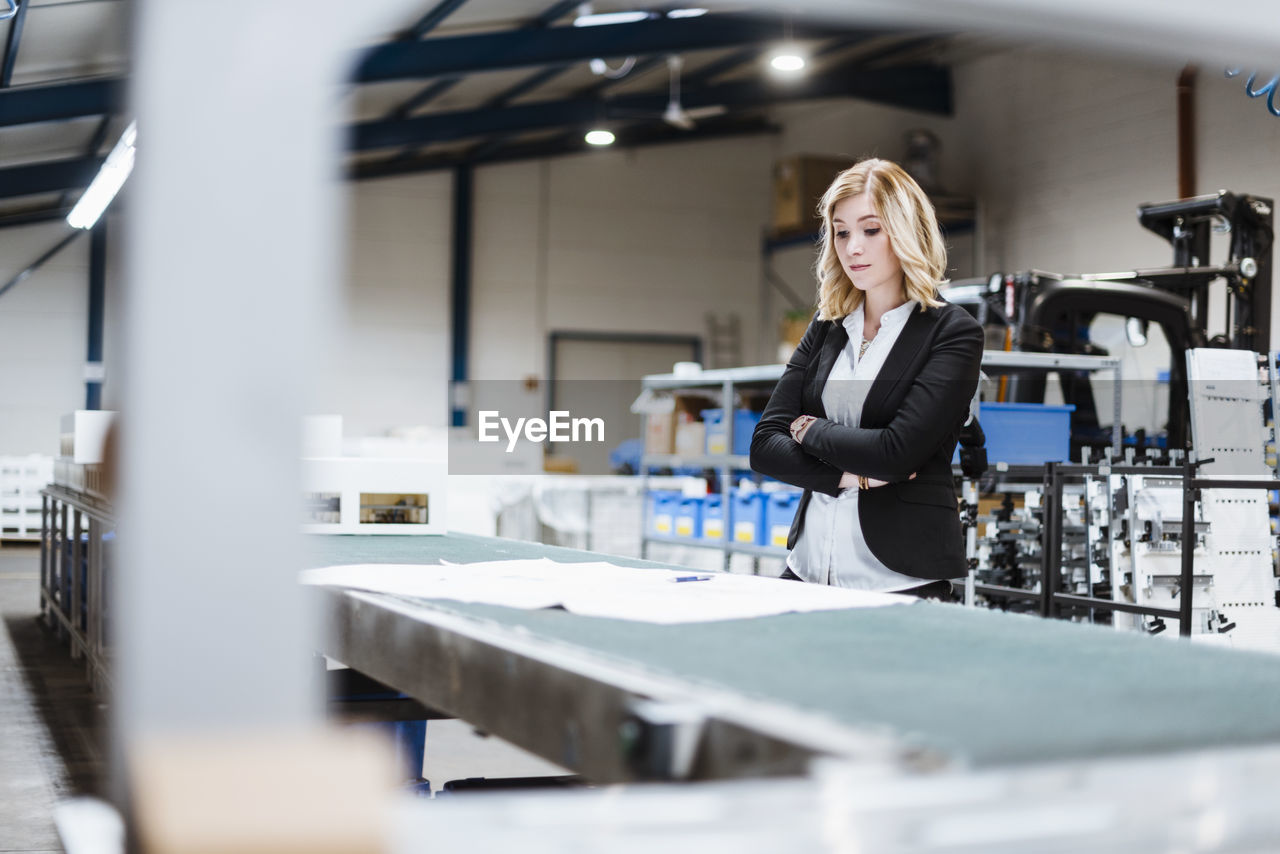 Blond businesswoman standing on shop floor, looking at plans