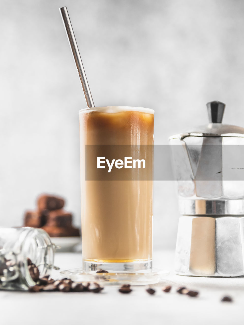 Close-up of iced coffee on table with moka pot, chocolate cake, coffee beans against concrete wall