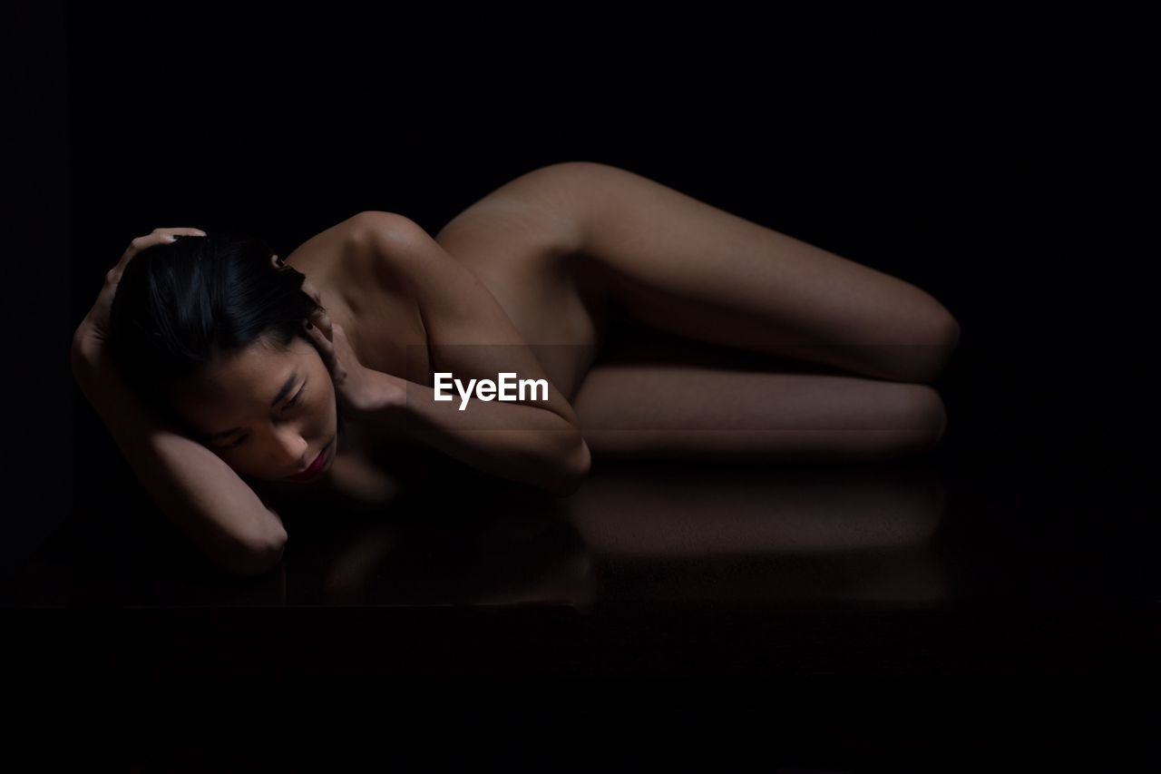 Naked woman lying over black background