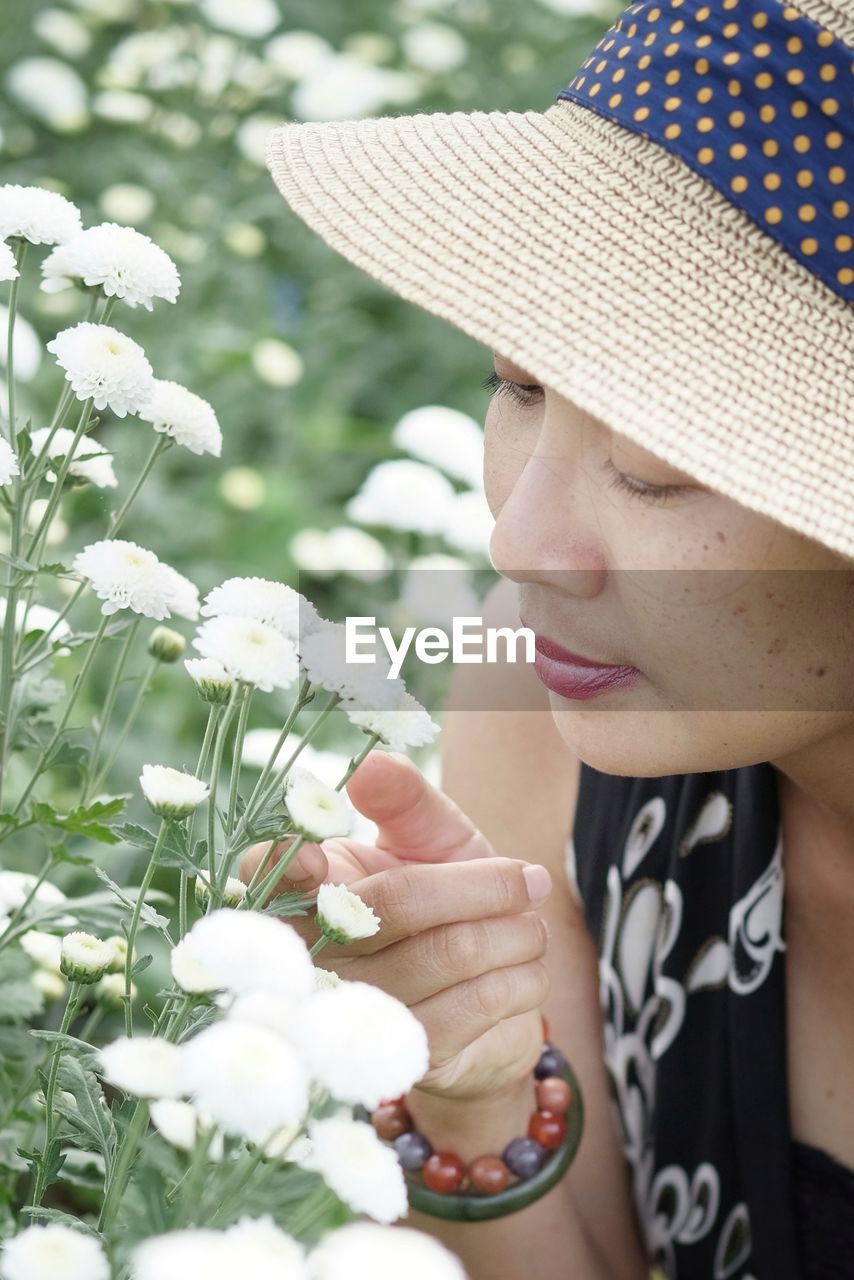 Close-up high angle view of woman wearing hat while looking at white flowering plants