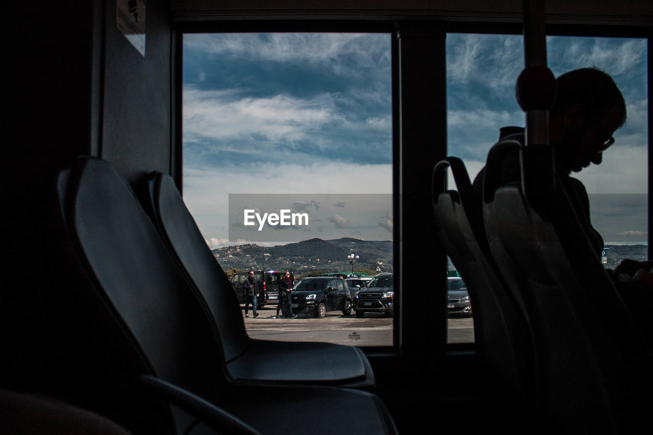 Man sitting with people seen through window against sky