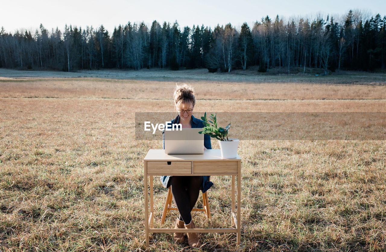 Travelling woman working on a laptop and desk in a field outside