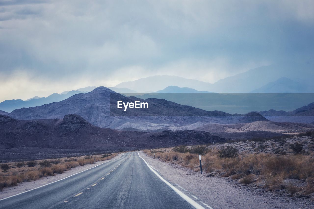 Road leading towards mountains against sky