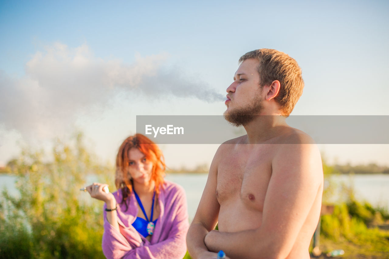 Young man smoking cigarette against woman