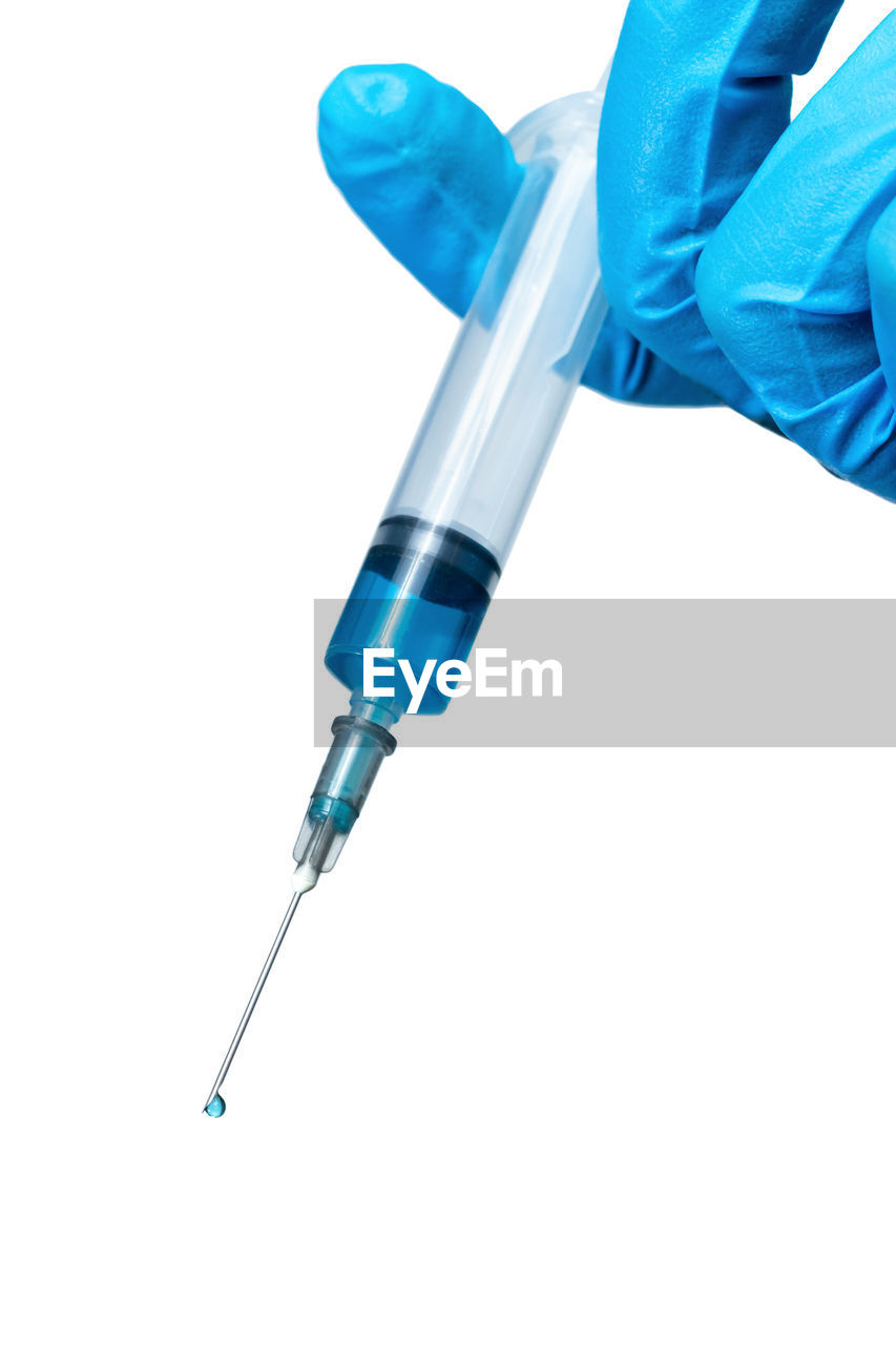 Close-up of hand holding syringe against white background