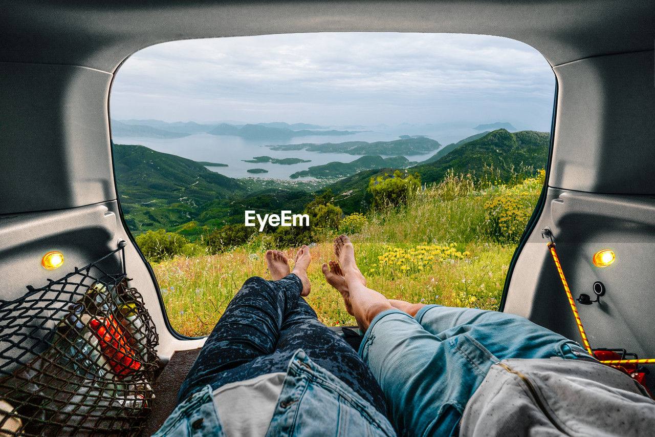 People relaxing in car trunk against mountain and sea