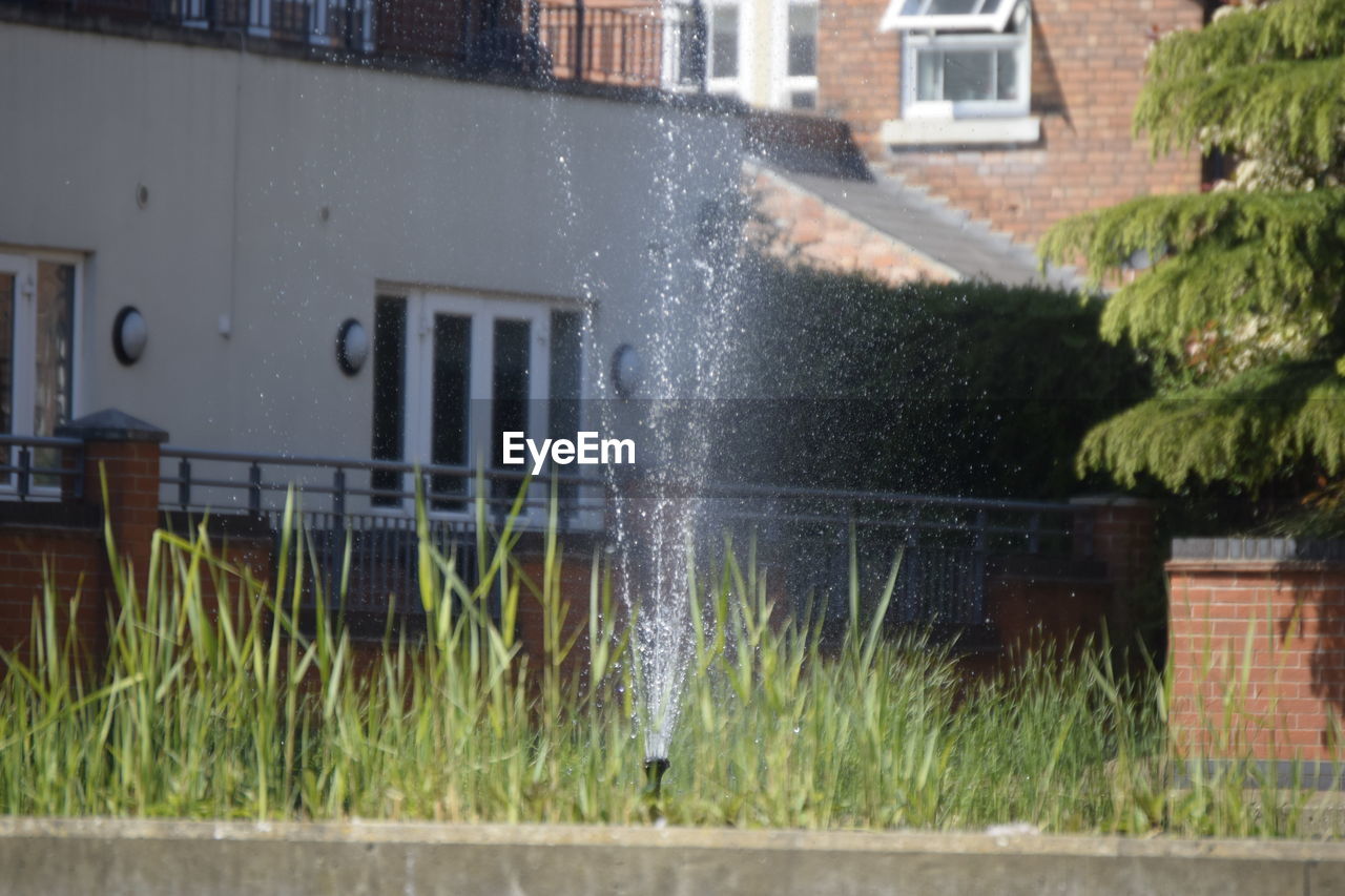 Sprinkler splashing water on grass by building