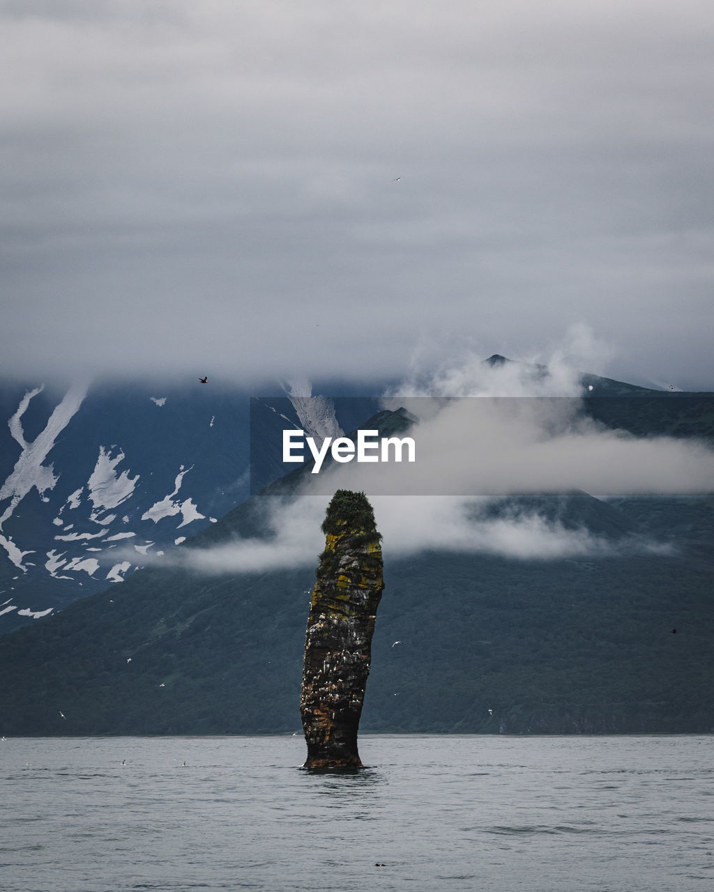 Stack rock in sea with mountains in background