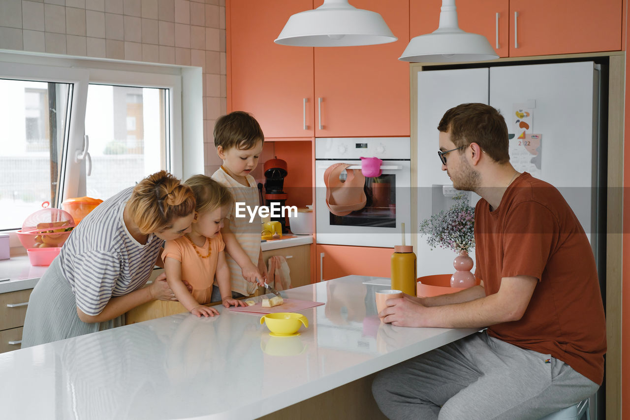 Happy family with kids cooking on modern kitchen. children cutting fruit salad, preparing food with