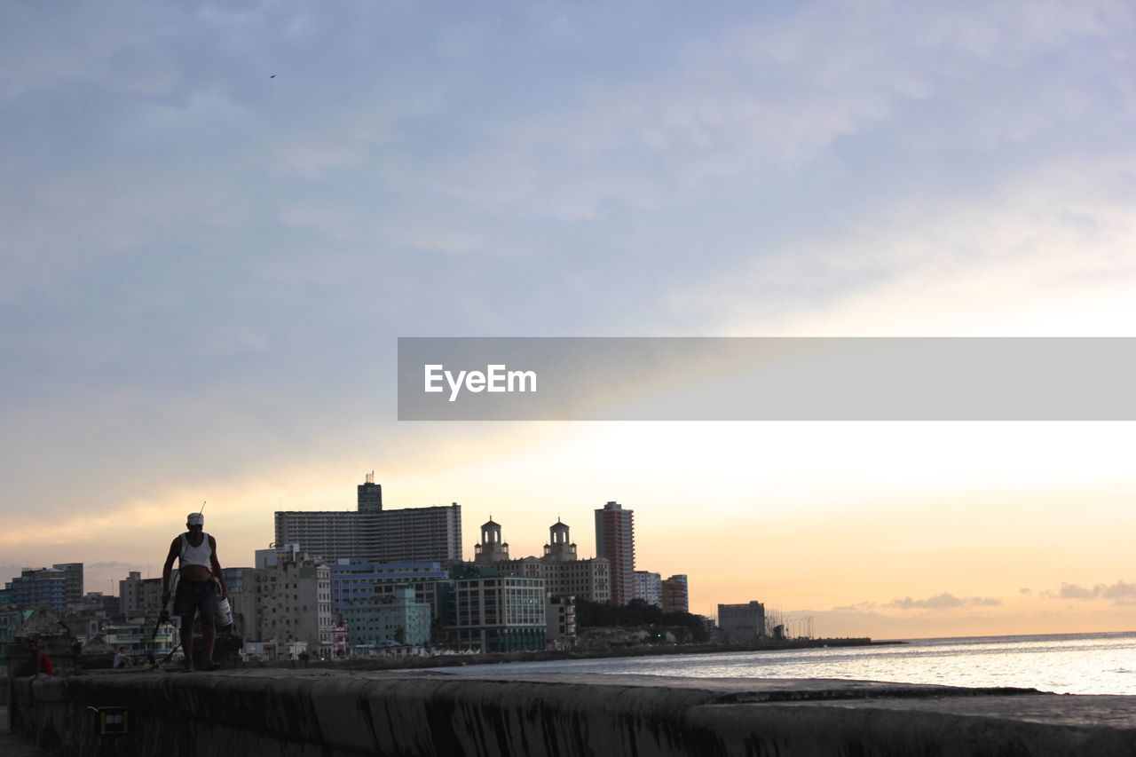 Modern cityscape by sea against sky during sunset