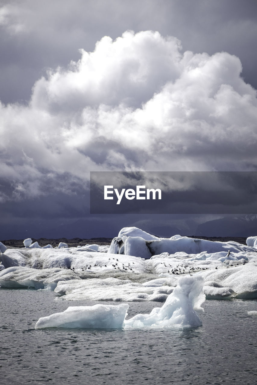 Glaciers in sea against cloudy sky