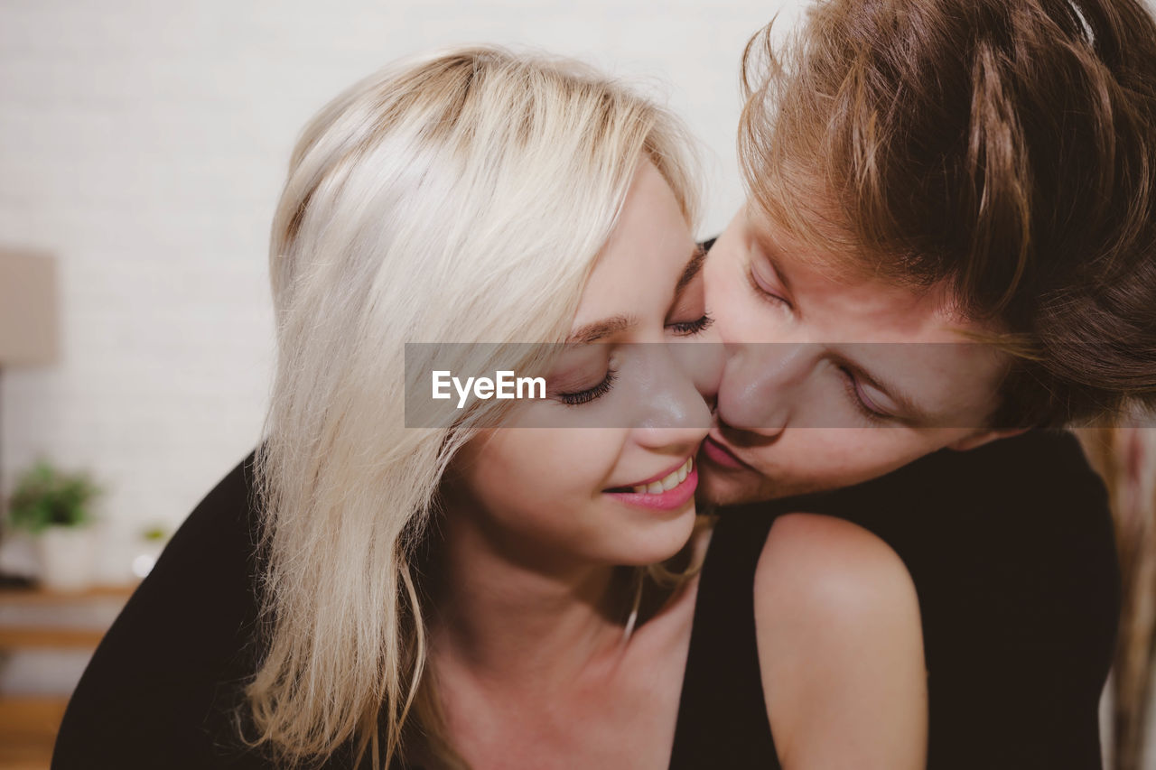 Close-up of man kissing girlfriend on cheek at home