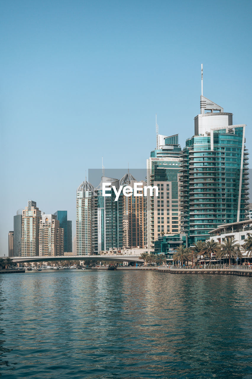 Buildings by river against clear sky