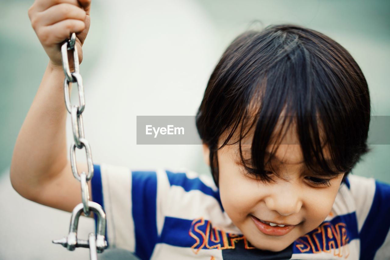 Close-up of smiling boy swinging in playground