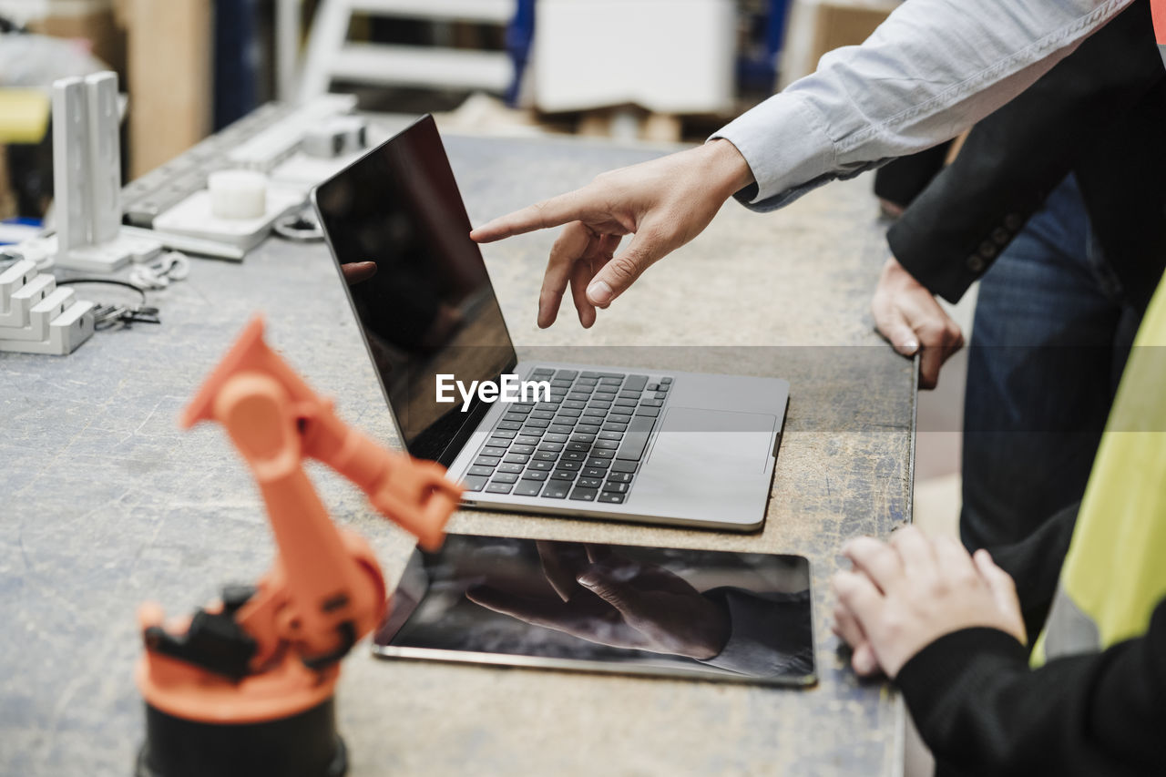 Hand of businessman pointing on laptops screen with colleagues at industry