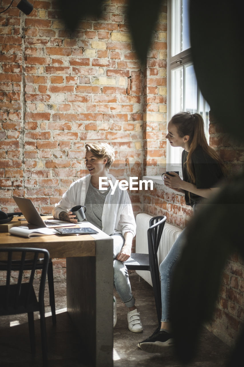 Female colleagues having coffee while using laptop startup company