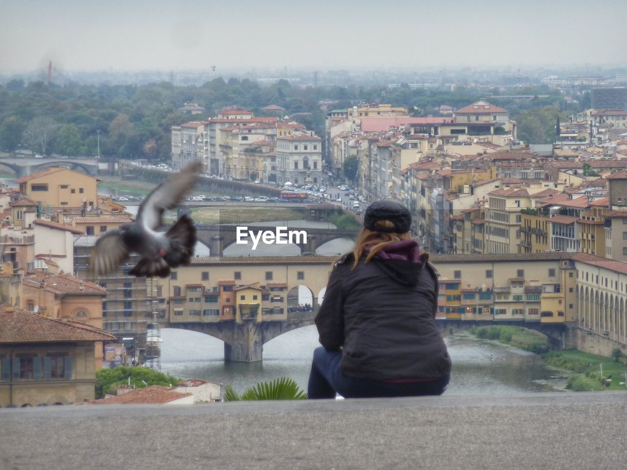 REAR VIEW OF WOMAN SITTING ON BRIDGE