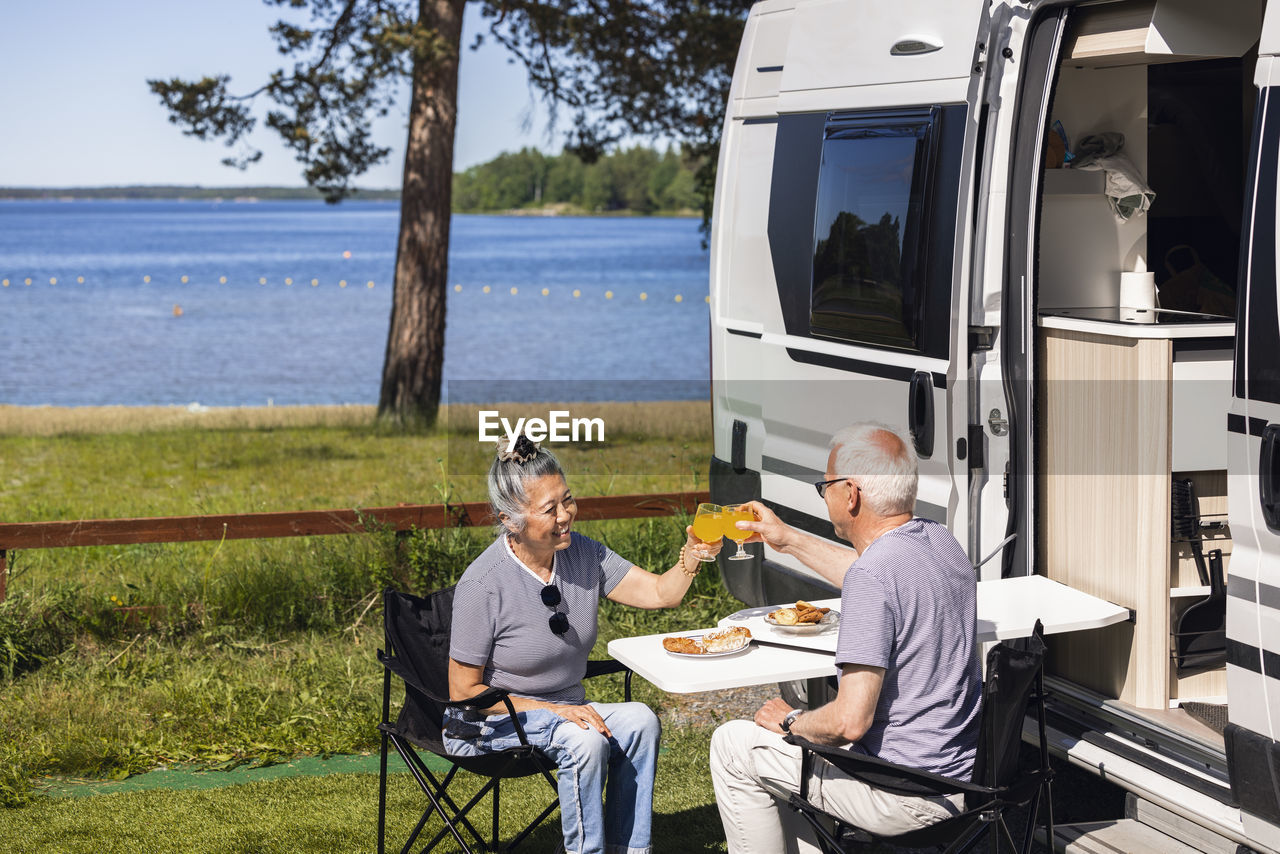 Senior couple having meal and rising toast at camp site