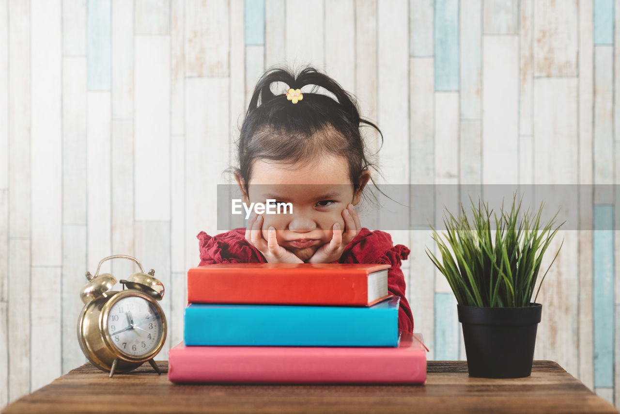 Little asian girl with moody face sitting against table with books.