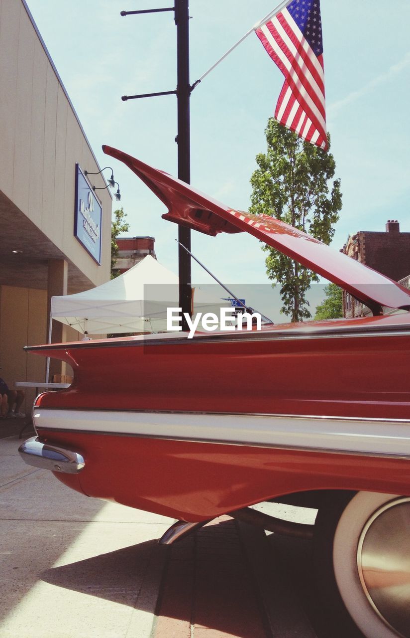Cropped image vintage car by american flag on pole against sky