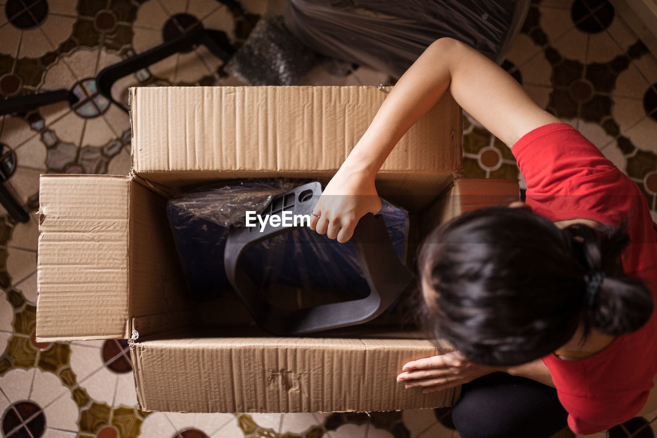 Top view of anonymous female taking parts of chair from carton box before assembling furniture at home