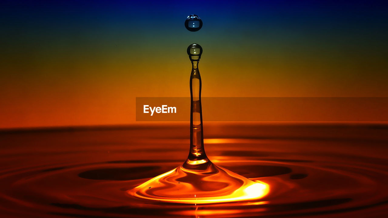 CLOSE-UP OF DROP FALLING ON WATER IN ORANGE SUNSET