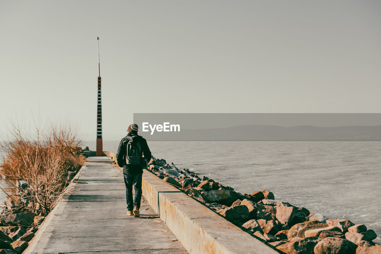 Rear view of man walking on pier against clear sky