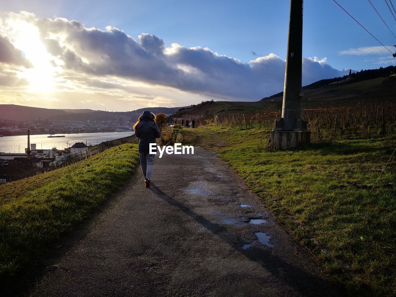 MAN WALKING ON ROAD AGAINST SKY