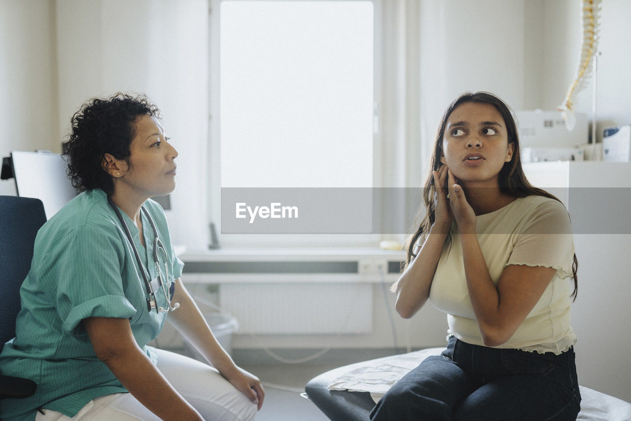 Young woman showing ear to female physician while sitting in clinic