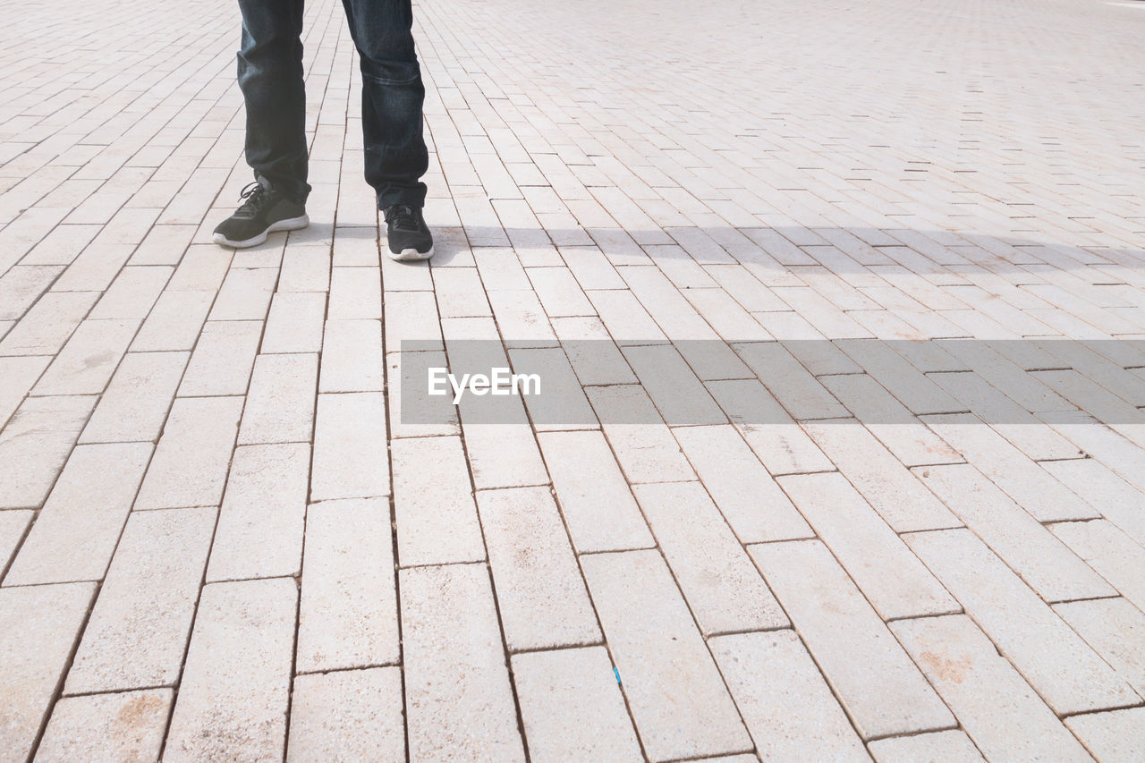 Low section of man standing on footpath during sunny day