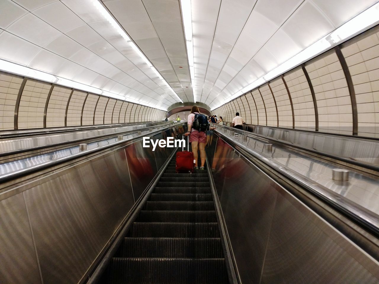 Rear view of woman with luggage standing on escalator in airport