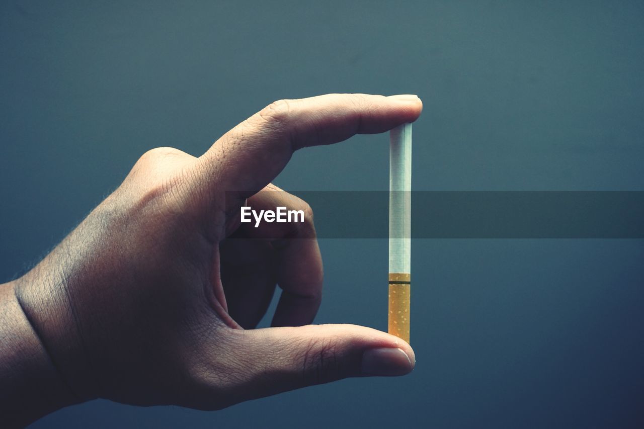 Cropped hand holding cigarette against gray background