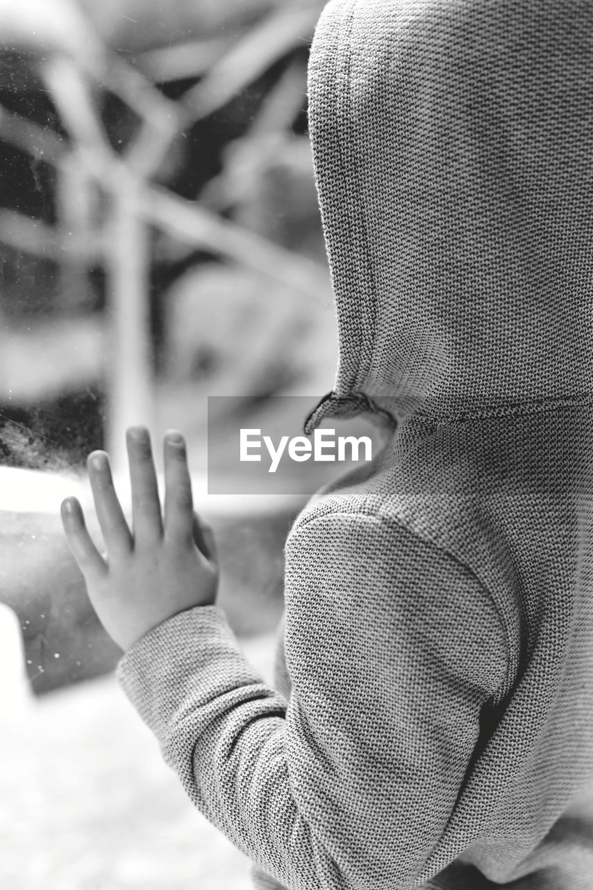 Boy wearing hooded shirt looking through window at home