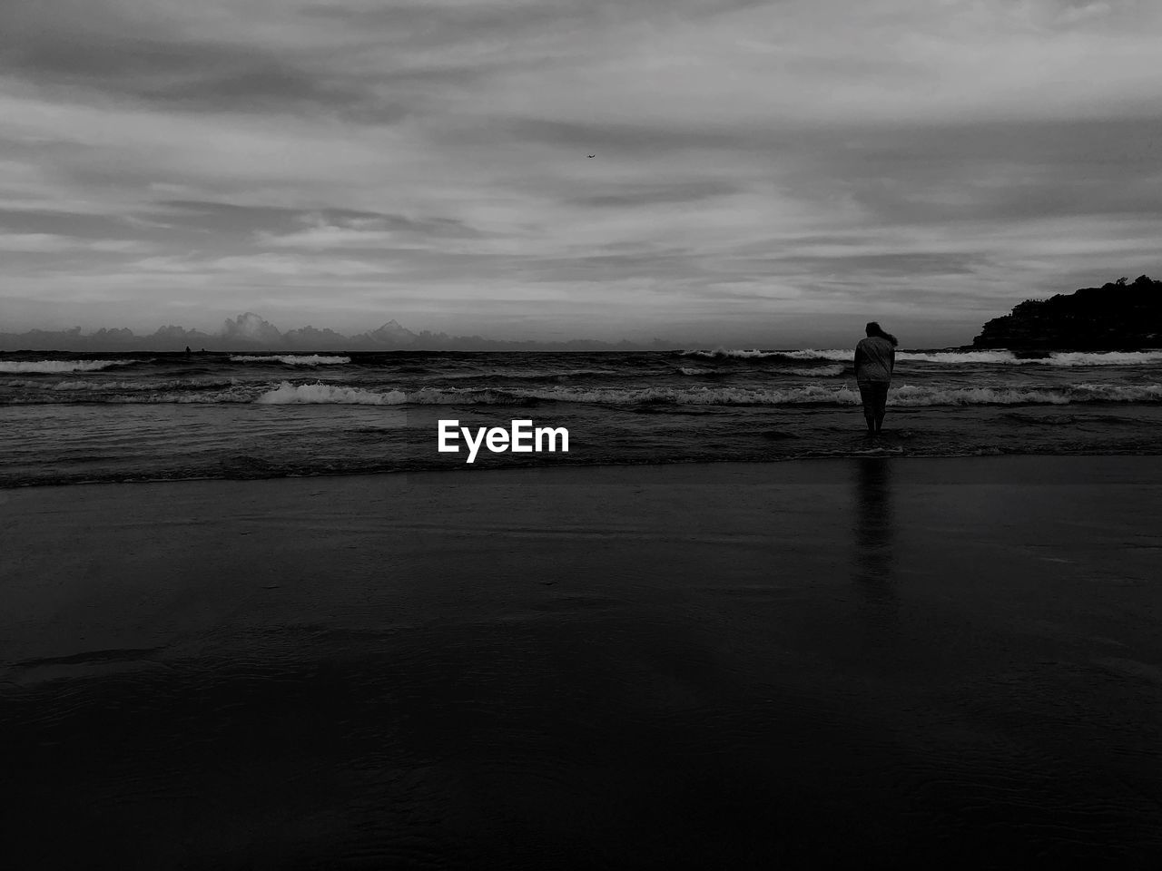 Rear view of woman standing at beach against cloudy sky