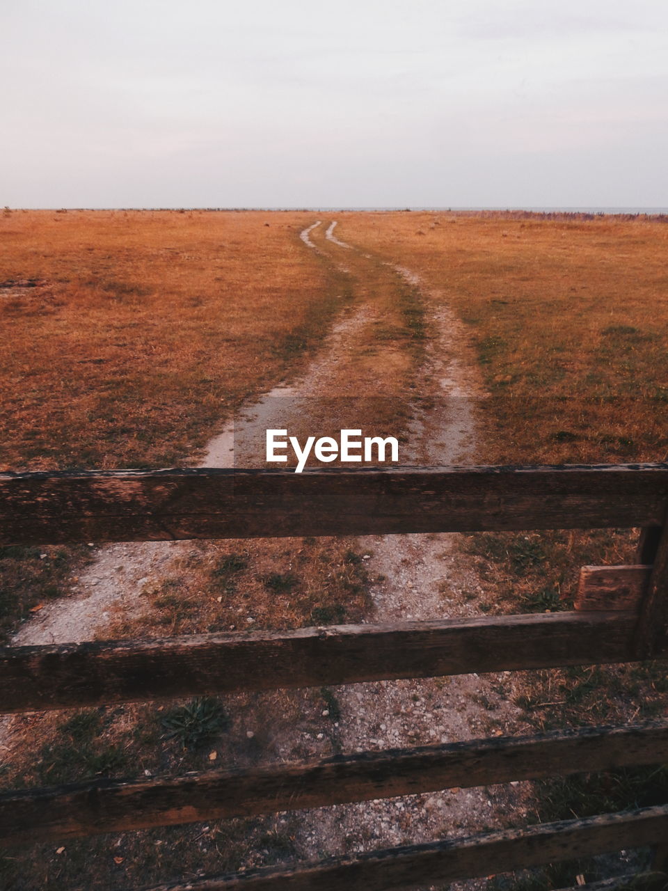 Wooden fence by road on field against sky