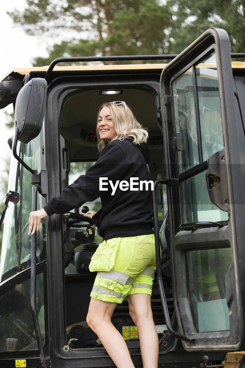 Smiling young woman getting in excavator