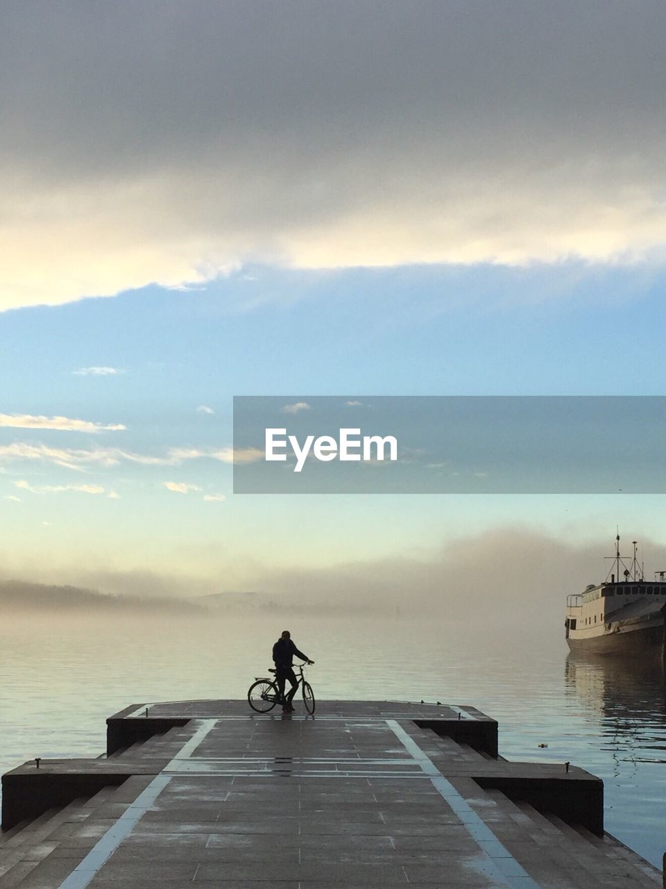 MAN CYCLING ON SEA AGAINST SKY