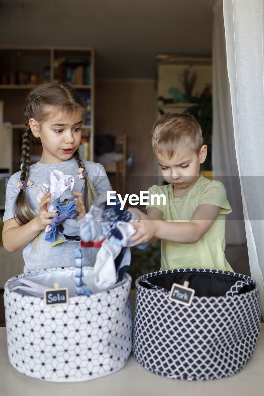 Cute sibling putting clothes in container