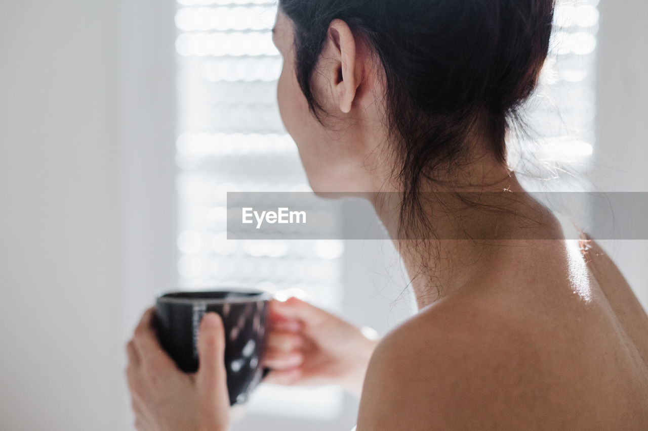 Midsection of woman sitting on bed while holding coffee cup at home